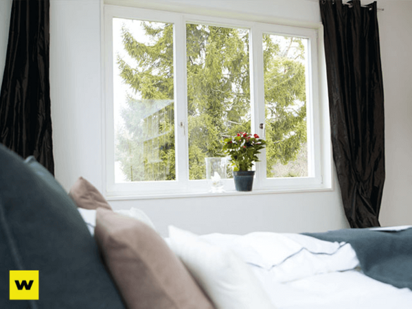 Helles Schlafzimmer mit großem Fenster, Blick ins Grüne, Pflanzen und gemütlicher Bettwäsche.