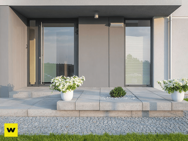 Moderner Hauseingang mit großen Glasflächen, Steinplatten und dekorativen Blumenkübeln.