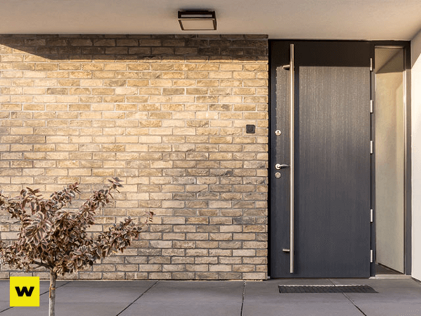 Moderne Haustür aus Aluminium vor heller Klinkerfassade mit kleinem Baum im Eingangsbereich.